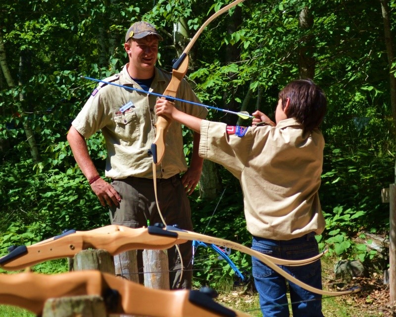 A Scout shooting a bow and arrow while a staff member observes them from the side