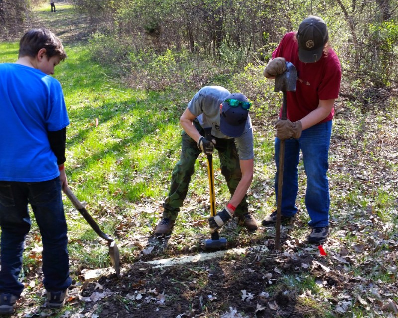 Three Scouts using shovels to work on a project in a field