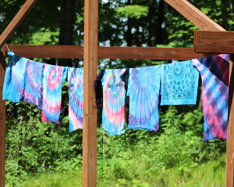 A line of freshly tie-dyed shirts and bandanas on a clothesline in the sun