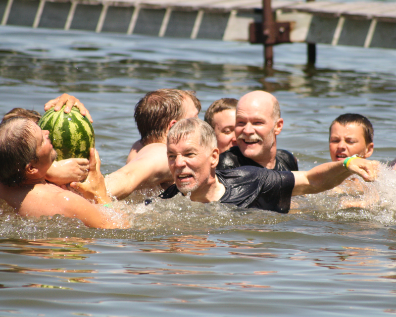 A group of Scouts and adult leaders swimming and smiling as they fight over a watermelon in the lake