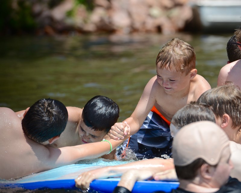 A group of younger Scouts swimming. One Scout is grabbing the hand of another to help them up