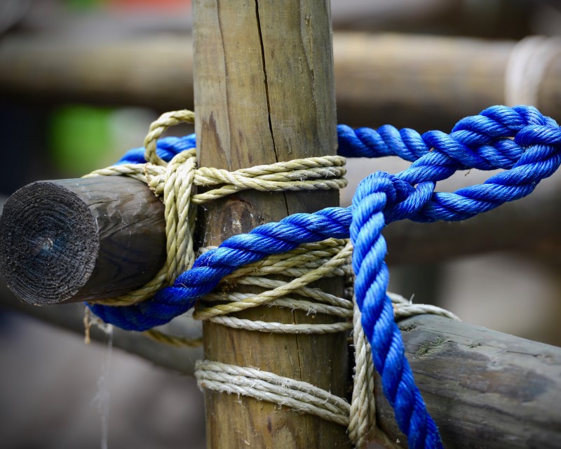 Two poles square lashed onto a pole in the ground with quarter-inch rope. A trucker's hitch is tied around all three poles with half-inch rope