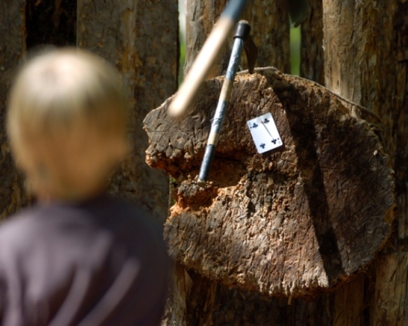 A mid-air Tomahawk thrown by a young Scout towards a playing card pinned to a log