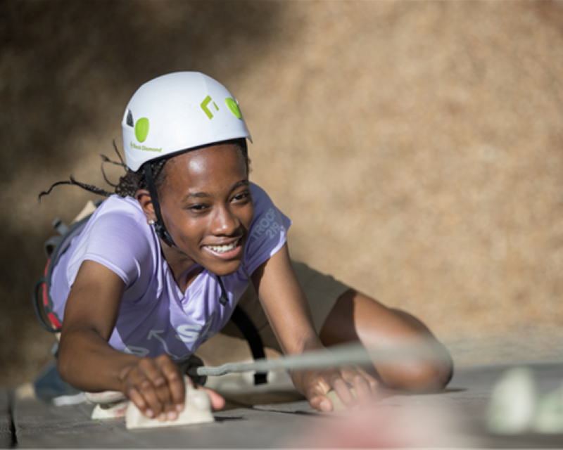 Looking down on a Scout wearing a helmet and harness climbing up the wall from the top of the tower